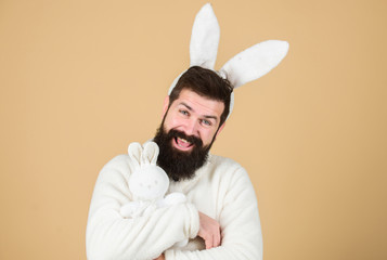 Naklejka premium Easter rabbit is a symbol of Easter and spring season. Happy hipster with long rabbit ears holding bunny toy. Bearded man in easter rabbit costume with hare toy. Fertility and new life. Easter eve