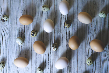Lots of chicken and quail eggs on a plain wooden background.