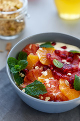 Bowl of homemade granola with yogurt, citrus and pomegranate seeds on gray wooden background. Selective focus. Healthy eating or vegetarian food concept