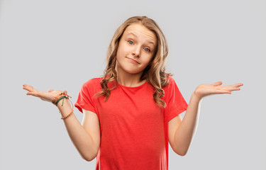 people, emotion and expression concept - wondering teenage girl in red t-shirt shrugging over grey background