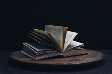 One open old book on a round wooden table. Beautiful dark background...