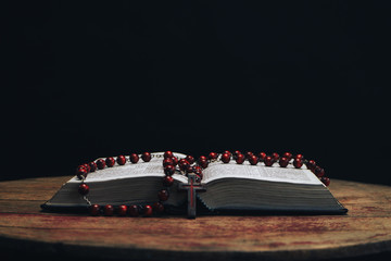 Bible and the crucifix beads on a old round table. Beautiful night background. Religion concept...