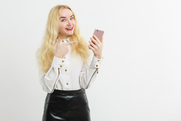 Smiling woman is pointing on smartphone standing on white background.