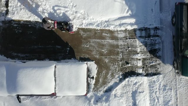 Aerial top view of man using snow blower on driveway.