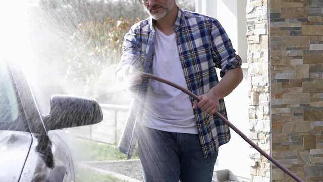 Man Washing Car With Hose In Driveway