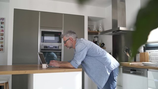 Relaxed man on computer at home in modern kitchen