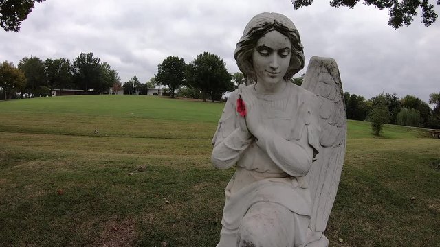 This is a slow motion approach towards a statue of a praying Angel. Someone had stuck a flower between its hands.
