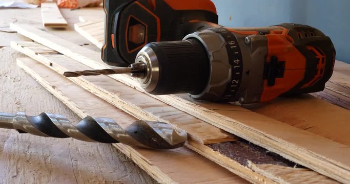 A power tool drill on a stack of plywood lumber boards with a drill bit on a construction site.