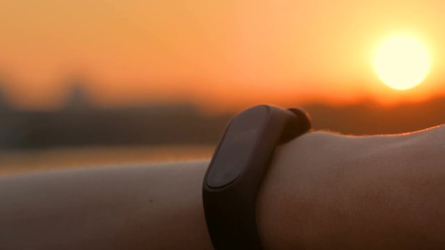 Woman using wearable fitness tracker device on city quay. Sunset light, golden hour. Technology and entertainment concept
