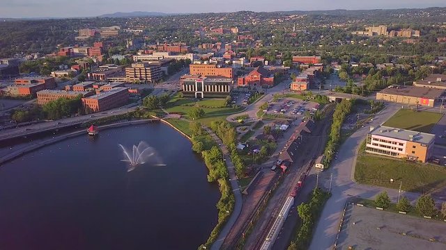 Drone moving backwards near downtown, over the lake, with buildings and train rails - summer season.