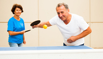 Happy mature man and woman playing table tennis