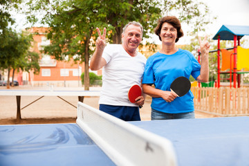 mature couple showing victory near table tennis