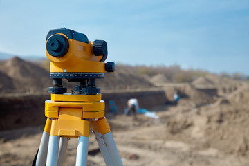Special device (level) for surveyor builders, geodesy equipment close up in front of a ground work with people on blurred background. Outdoors, copy space. - obrazy, fototapety, plakaty