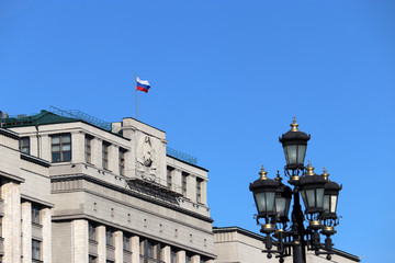 Russian flag on the Parliament building in Moscow against blue sky. Russian authority, facade of State Duma of Russia with soviet coat of arms