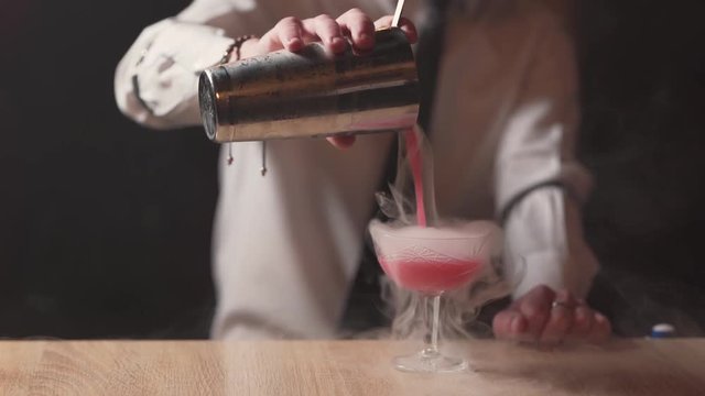 Professional bartender pouring smoking drink into a glass