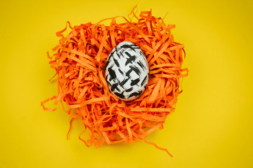 top view dyed black and white easter egg with geometric patetrn in decorative nest  on a yellow background