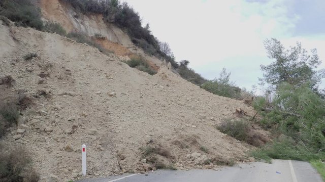 Close-up pan over a huge pile of dirt blocking passage through a mountainside road after a landslide
