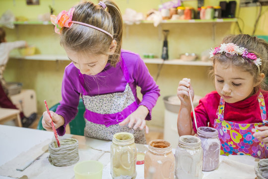 Two Little Girls At Pottery Workshop Painting Clay Vase