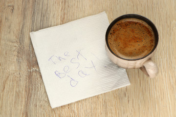 mug with coffee and a pen on a napkin with the inscription The Best Day