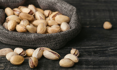Roasted pistachios  in gray bag on textured  dark wooden background, top view. Copy space. 
