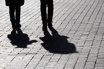 Silhouettes of two people walking down the street. Couple outdoors, people shadows on pavement, concept of dramatic stories