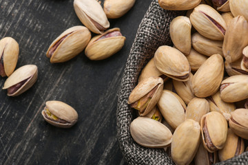 Roasted pistachios  in gray bag on textured  dark wooden background, top view. Copy space. 