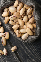 Roasted pistachios  in gray bag on textured  dark wooden background, top view. Copy space. 