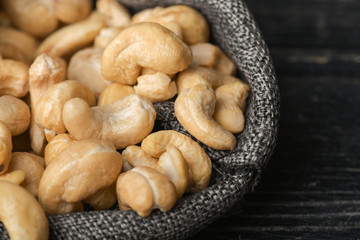 Cashew nuts in gray bag on textured  dark wooden background, top view. Copy space. 