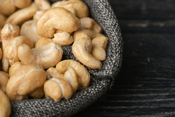Cashew nuts in gray bag on textured  dark wooden background, top view. Copy space. 