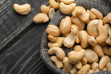 Cashew nuts in gray bag on textured  dark wooden background, top view. Copy space. 