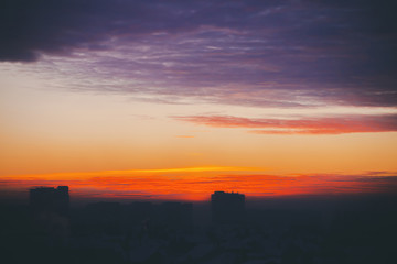 Cityscape with wonderful varicolored fiery dawn. Amazing dramatic multicolored cloudy sky. Dark silhouettes of city building roofs. Atmospheric background of sunrise in overcast weather. Copy space.