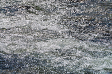 Natural texture of foamed water surface. Rapids of river close-up. Fast flow in mountain creek. Background of clean water waves with copy space. Textured foam of shiny stream. Fast river texture.