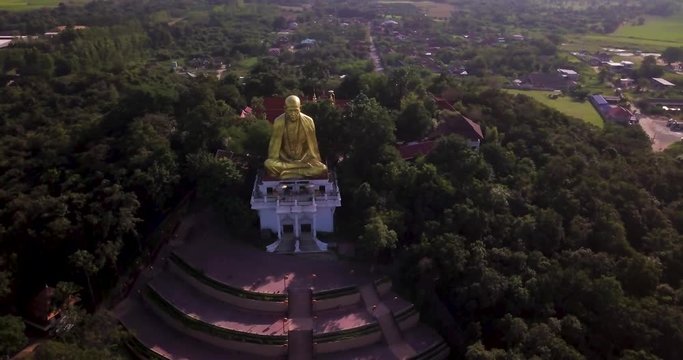 Drone circling around a huge golden buddha monument on the top of a hill. Lamphun, Thailand.