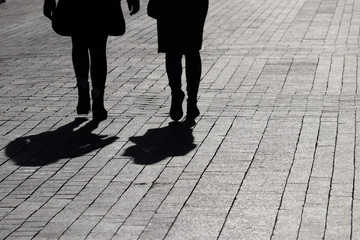 Silhouettes and shadows of two women walking down the street. People outdoors, concept of female...