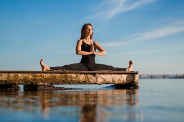 Fototapeta na wymiar Young woman practicing yoga exercise at quiet wooden pier with city background. Sport and recreation in city rush