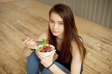 Sports beautiful girl sitting on the floor and eating a salad from fresh vegetables and greens. Healthy lifestyle.