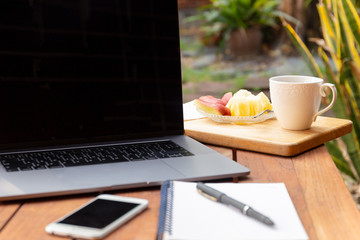 Coffee mug with fresh fruit and laptop on wooden table in the garden.