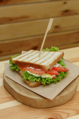 juicy sandwich with bacon, fresh vegetables, green salad and dark lines after grill on wooden plate