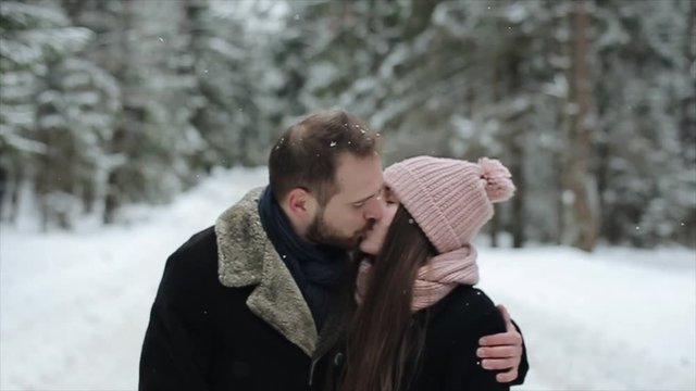 Young attractive couple walking andkissing in a winter forest under heavy snow. Slow motion.