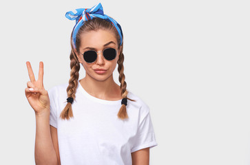 Studio portrait of cheerful blonde young woman wearing trendy sunglasses, white t-shirt and blue...