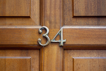 House number 34 on an unpainted natural wooden door in metal numerals with natural wood grain showing