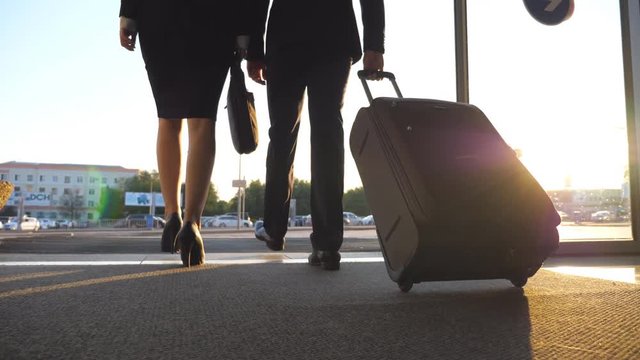 Business man and woman with luggage going from the airport to city street. Follow to young businessman carrying suitcase on wheels and walking with his female colleague from terminal hall. Slow motion
