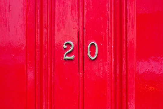House number twenty with 20 in bronze numbers on a red wooden door