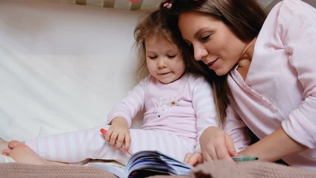 Caring young mother teaches her daughter to paint the coloring correctly. The concept of a happy childhood and development activities