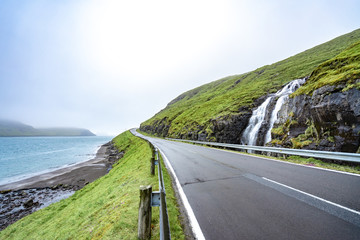 Amazing view of road beside the ocean with waterfall and green grass in Faroe Islands, noth Atlantic ocean, Europe, hidden jem for travel destination
