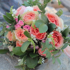 Bridal bouquet lying on the stones. Wedding bouquet of peach roses by David Austin,  single-head pink rose aqua, eucalyptus, ruscus, gypsophila