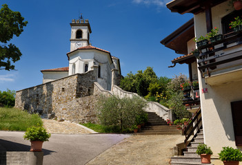 Fototapeta premium Entrance way to the white stucco catholic church of Saint Leonard with chain and clock belfry in Dolnje Cerovo Gorica Hills Brda Slovenia