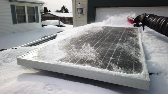 Someone brushing snow off of a solar panel that is mounted on top of an SUV at half speed