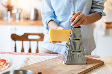 Woman grates cheese with grinder. Family is cooking pizza and homemade italian food in kitchen. Lifestyle moment.