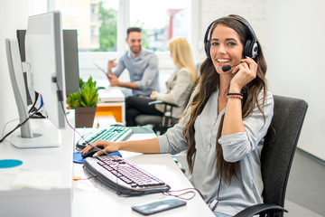 Attractive young business woman with headset working in call center. - obrazy, fototapety, plakaty